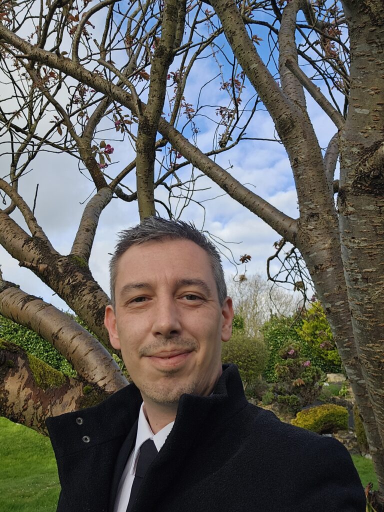 An image of me, Tomos James, a funeral celebrant, standing in front of a tree.